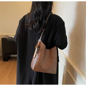 Détail du sac à bandoulière en cuir marron avec breloque perlée et sangle latérale