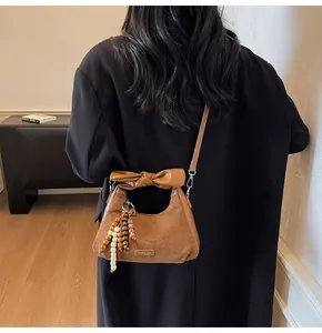 Brown dumpling bag with bow detail and beaded pendant worn by a model in a home setting