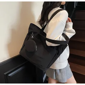Detail of black nylon tote bag featuring side pockets and a small round coin purse attachment
