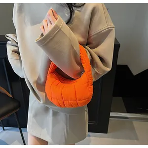 Close-up of bright orange quilted crescent handbag with puffer texture on shoulder