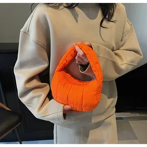 Detailed view of bright orange quilted puffy bag with metallic zipper and crescent shape