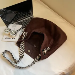 Dark brown suede tote bag with striped shoulder strap and lifestyle desk accessories