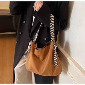 Detail of brown suede tote bag featuring a decorative black and white striped rope strap