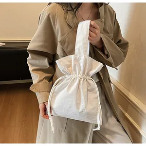 Detail van witte canvas handtas met trekkoord die textuur en gevouwen vorm toont