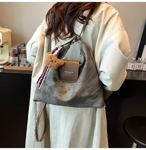 Détail du sac hobo gris foncé avec rabat en cuir marron, chaîne et breloque ourson