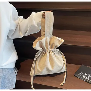 Detail van de minimalistische beige bucket bag met trekkoord op houten traptreden