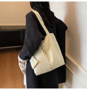 Detail view of large cream nylon tote bag with front pocket shown on shoulder