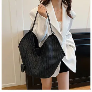 Dettaglio borsa shopper nera intrecciata con ciondolo a cuore su blazer bianco elegante