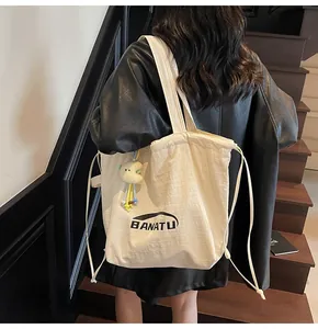 Detail of cream drawstring canvas tote with cloud plush charm and BANATU logo on back