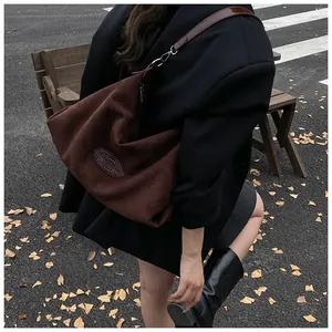 Detail of deep brown suede hobo bag shown on shoulder in an outdoor urban autumn setting