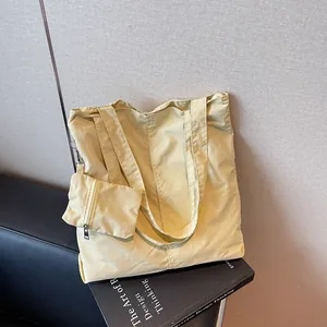 Pale yellow large capacity nylon tote bag with matching zipper pouch on a leather seat