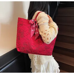 Dettaglio della borsa tote in jacquard rosso con ricami floreali e ciondolo a fiocco