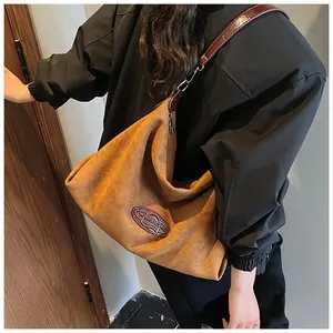 Detail view of large brown suede tote bag featuring oval leather patch and slim shoulder strap