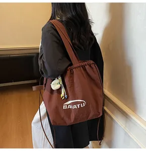 Detail of dark brown drawstring nylon tote bag featuring white logo and plush cloud charm