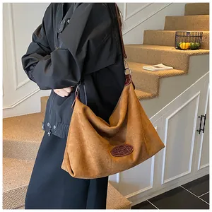 Detailed close-up of brown suede tote bag featuring oval leather logo and silver metal hardware