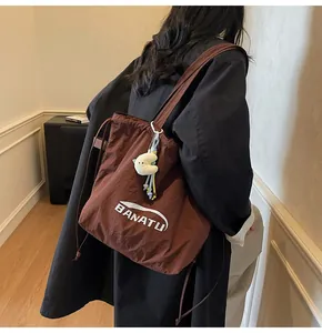 Detail of a brown nylon tote bag with drawstring closure and white moon plush pendant
