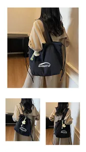Detail of black nylon drawstring tote bag featuring logo print and cute monster pendant