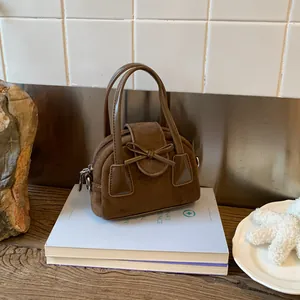 Detail of dark brown suede mini handbag with decorative bow and top handle on books