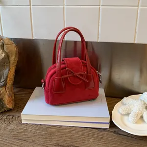 Detail of red faux suede handbag with bow decoration and smooth metal zipper closure