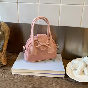 Close-up of pink crossbody bag with bow decoration and matte suede texture on books