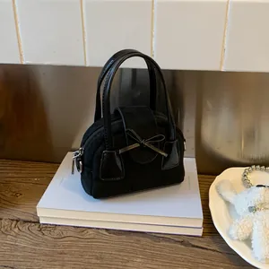 Close-up of black mini crossbody bag with suede texture and leather bow detail