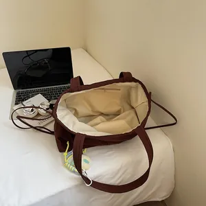 Deep brown canvas tote bag with large capacity, inner zipper pocket and woven charm detail