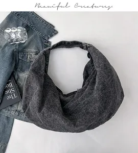 Flat lay of gray washed denim hobo bag with a crescent shape and lifestyle props