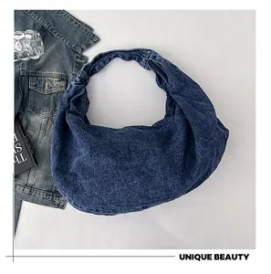Flat lay of a large blue denim hobo bag styled with a jacket and magazine on white back