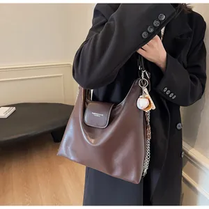 Macro shot of dark brown oily leather tote featuring metal chain strap and charm