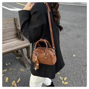 Brown suede boston bag with wooden bead charm worn by model in an autumn street scene