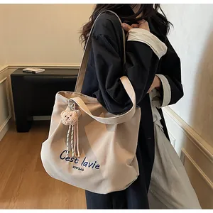 Zijaanzicht van beige canvas bucket bag met C'est la vie borduursel en pluche berenbedel