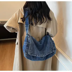 Detailed back view of a large vintage blue denim crossbody bag worn over a beige coat