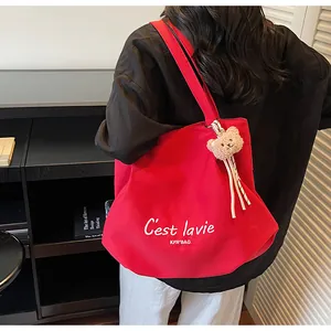 Detail van de rode canvas shopper met witte letters en een bruine pluche beer sleutelhanger