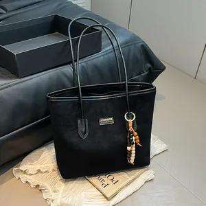 Chic black tote bag with beaded pendant charm shown in a high-fashion lifestyle setting