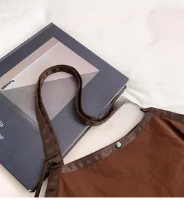 Detail of brown canvas tote bag with adjustable strap and green metal button closure