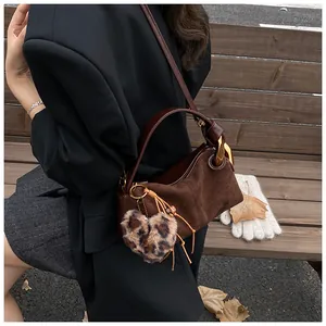 Detail view of brown suede crossbody bag with leopard heart charm and autumn leaves background