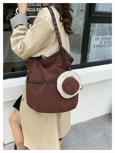 Detail of a large brown canvas tote bag featuring a cute straw hat pendant and knot strap