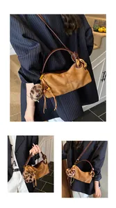 Macro detail of brown suede shoulder bag with gold chain strap and leopard pompon charm