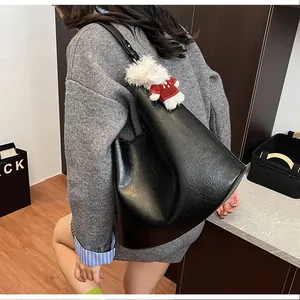 Detail of black large capacity tote bag with glossy texture and plush dog pendant