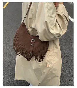 Détail d'un sac bandoulière marron à franges avec boucle et manteau beige élégant