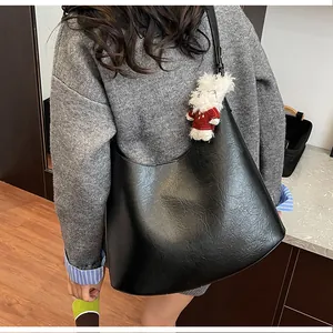 Detail of black pleated shoulder bag with texture and a cute white teddy bear charm