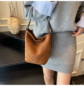 Detail of a brown suede bucket bag featuring a sleek leather strap and gold metal hardware