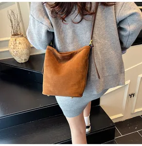 Detail of brown suede bucket bag featuring golden bottom studs and adjustable strap