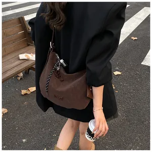 Detail of dark brown matte hobo bag featuring woven rope charm and leather logo patch