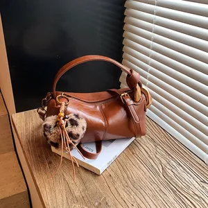 Brown vintage pillow shoulder bag with golden buckles and leopard heart charm on wood base