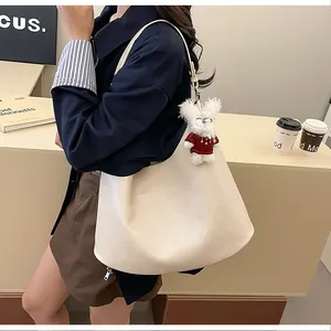 Detail of cream large tote bag featuring textured leather and a plush bear pendant