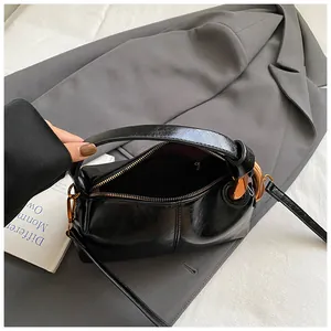 Glossy black leather crossbody pillow bag with gold hardware on grey suit background
