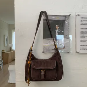 Detail of dark brown suede half-moon bag featuring contrast stitching and tassel charm