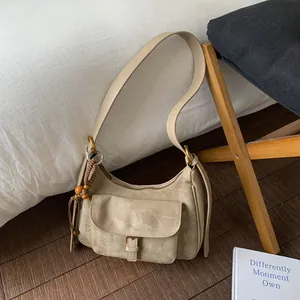 Beige suede shoulder bag with flip-pocket and ethnic charm on a white bed