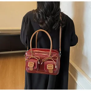 Detailed view of deep red glossy shoulder bag with bow ties and front pockets